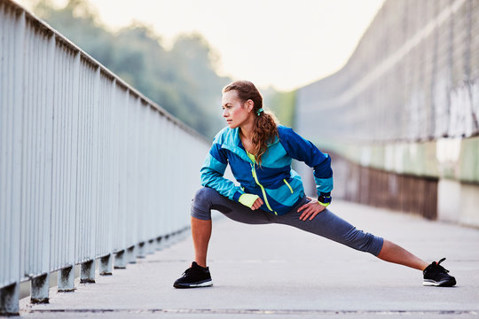 Young Woman Runner Stretching Legs During Morning Run