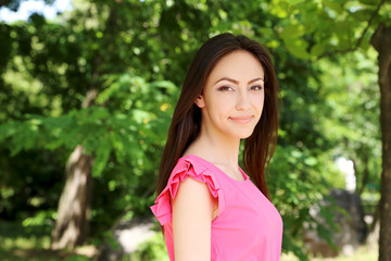 Fototapeta premium Young beautiful woman in pink dress standing in the park
