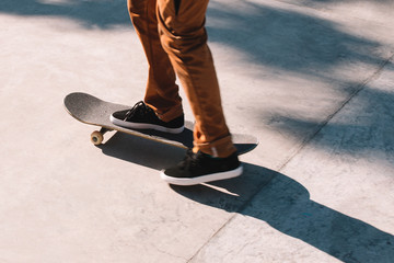 Close up of skater's legs in black sneakers on a skateboard in a concrete skatepark