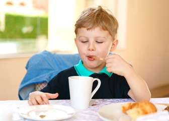 Small blond boy enjoys his breakfast, sitting at a table in a resort cafe.