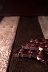Chocolate pieces with hazelnut nuts on wooden background.