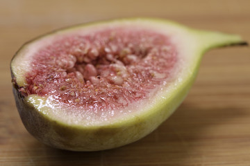 Fig cut in half on a wooden background. This is a macro photograph with the focu being the foreground of the fruit.