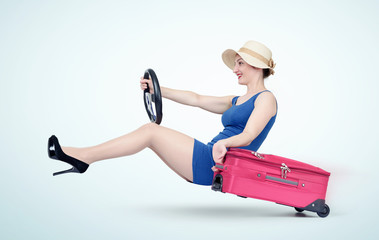 Beautiful girl in blue dress with pink suitcase drives a car. Lady goes on vacation