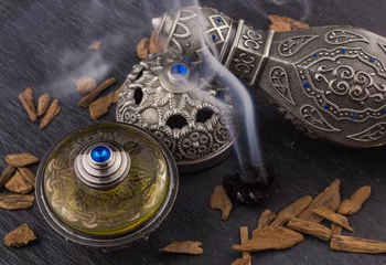 Fototapeten Silver Oriental Artisitc Arabian Oud Perfume / Arabian Oud Perfume with Oud Scented Wood burned in the background with Scented Smoke in the Air  © bassemadel