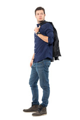 Fototapeta premium Young smart casual man walking while carrying jacket over shoulder looks back. Full body length portrait isolated over white studio background. 