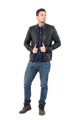 Fototapeta premium Confident young man pulling leather jacket collar looking away. Full body length portrait isolated over white studio background. 