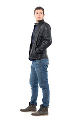 Side view of young man in leather jacket and jeans looking back over the shoulder. Full body length portrait isolated over white studio background. 