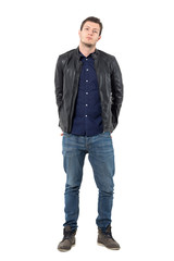Young man in leather jacket and jeans with hands behind back and titled head. Full body length portrait isolated over white studio background. 