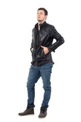 Young serious casual man in leather jacket with hands in pockets looking up. Full body length portrait isolated over white studio background. 