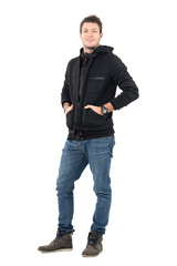 Young casual smiling man in hooded winter jacket with hands in pockets. Full body length portrait over white studio background.