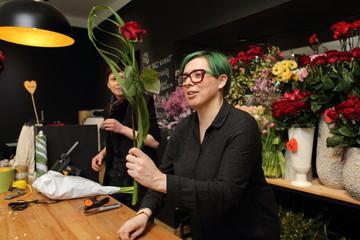 Kobieta w kwiaciarni pokazuje bukiet z kwiatów ciętych.