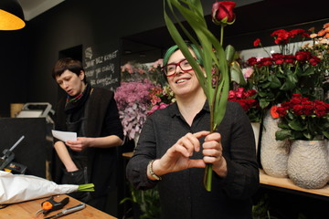 Kobieta w kwiaciarni składa bukiet z kwiatów ciętych. - obrazy, fototapety, plakaty