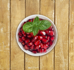 Pomegranate seeds on wooden background. Red grains of a pomegranate in ceramic bowl. Sweet and juicy garnet with copy space for text. Top view.