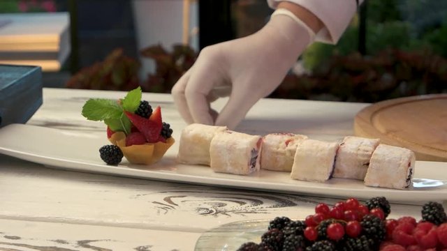 Plate with sweet sushi rolls. Mint leaf and berry pieces. Work of experienced pastry chef.