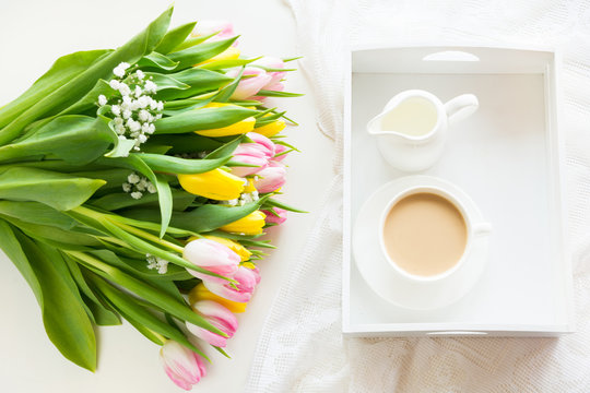Morning breakfast in spring with a cup of black coffee with milk in the pastel colors, a bouquet of fresh yellow and pink tulips on a white background. Top view.