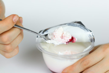 Girl's hand stirred with a spoon of natural yogurt and red jam. Yogurt on the spoon close up. Isolated on white background