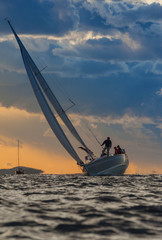 Sailing boat with crew on board during sunset