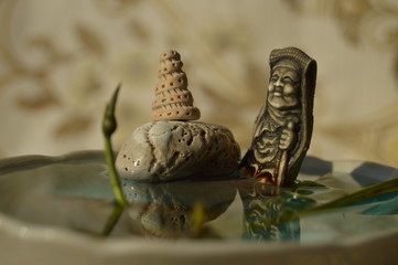  The statue is reflected in the water with a bud of the water lily. Blurred background
