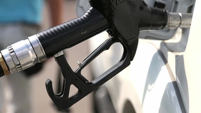 Fuel nozzle inserted in a car's gas tank as the car is being refueled at a gas station pump.