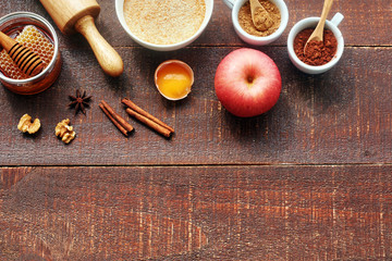 Baking ingredients for making apple cake. Fresh apple, flour, egg, honey, walnut, cinnamon, cocoa powder, brown sugar, roller pin over rustic wooden table. Copy space.