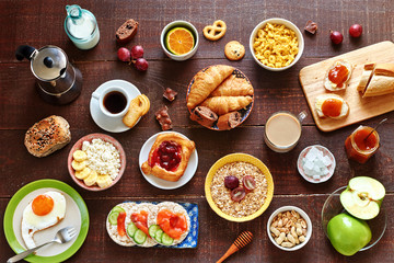 Fototapeta na wymiar Breakfast menu food frame with a copy space. Eggs, croissants, oatmeal with banana, cereal, danish pastry, crisps with salmon, apricot jam, fresh bread, chocolate, coffee and milk on a white table.