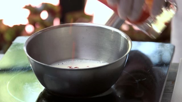 Chef preparing sauce. Tomato juice pouring into saucepan.