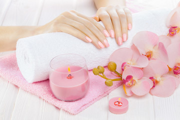 beautiful pink manicure with orchid, candle and towel on the white wooden table.