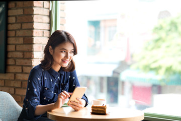 Beautiful cute asian young businesswoman in the cafe, using mobile phone and drinking coffee smiling