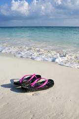 Fototapeta na wymiar Flip-flops on the beach of the Caribbean sea. Sunny and warm day at the shore. Relaxation and vacation. Vertical image.