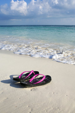 Flip-flops on the beach of the Caribbean sea. Sunny and warm day at the shore. Relaxation and vacation. Vertical image.