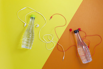 close up of water bottle and earphones on beautiful retro pastel color paper background,fitness background concept.