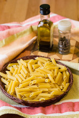 Raw penne pasta with olive oil and pepper on wooden table