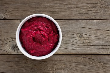 Bowl of fresh beet hummus, above view over a rustic wood background