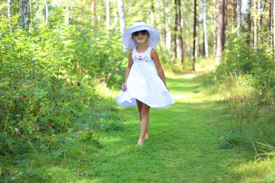 Sweet joyful girl in a hat running through the summer sunny forest