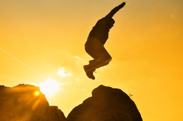 Silhouette the man jumping on top of the rock cliff mountain in sunset. Concept of successful man on top of the hill into the sun

