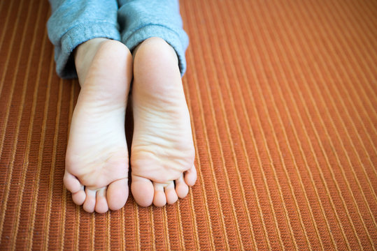 Sole of the feet of a boy on his knees on an orange carpet.
