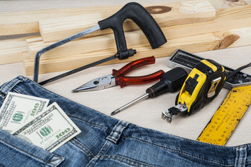 Construction and business concept .Different working tools, dollars in the pocket of jeans on wooden background.