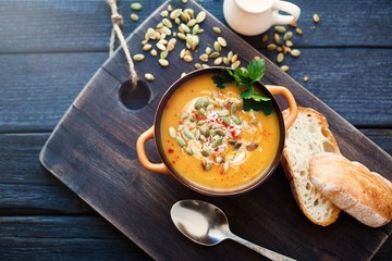 Homemade pumpkin soup with cream, bread, greens and pumpkin seeds on a wooden background. Top viev