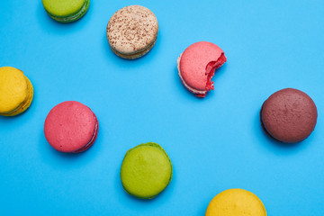 Top view of a bite colorful homemade macaroon lying among others on a blue flat lay