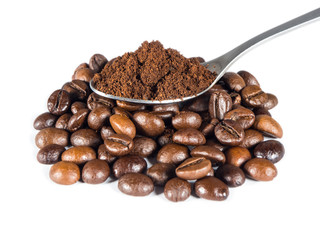 Spoon with ground coffee over pile of roasted beans on white isolated background