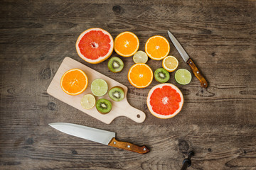 Slices fresh fruits on a brown table with cutting board and knives.