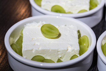 White desert bowl with cheep's cheese and green grapes as dessert before grilling in the oven