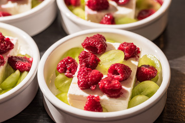 White dessert bowls with cheep's cheese, green grapes and red rasperries before grilling in the oven