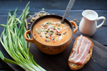 Homemade pumpkin soup with cream, bread, bacon and pumpkin seeds on a wooden background. Top viev
