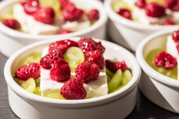 White dessert bowls with cheep's cheese, green grapes and red rasperries before grilling in the oven