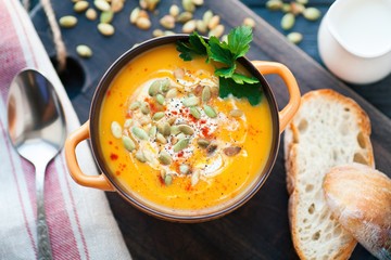 Homemade pumpkin soup with cream, bread, greens and pumpkin seeds on a wooden background. Top viev
