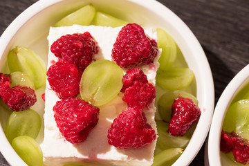 White dessert bowls with cheep's cheese, green grapes and red rasperries before grilling in the oven