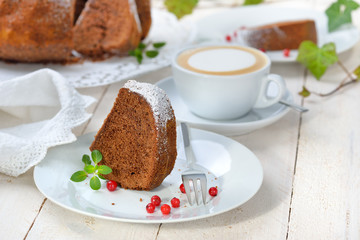 Schoko-Guglhupf mit  Zartbitterschokolade mit einer Tasse Cappuccino serviert - Freshly baked ring-shaped cake with chocolate, so called Gugelhupf in Austria and Germany, served with a cup of coffee