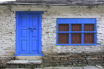 Fototapeta na wymiar Grunge gray bricks wall with blue door and window of Nepali house