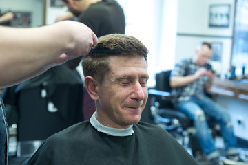 Smiling man, client in a barbershop, closing his eyes, enjoys the process